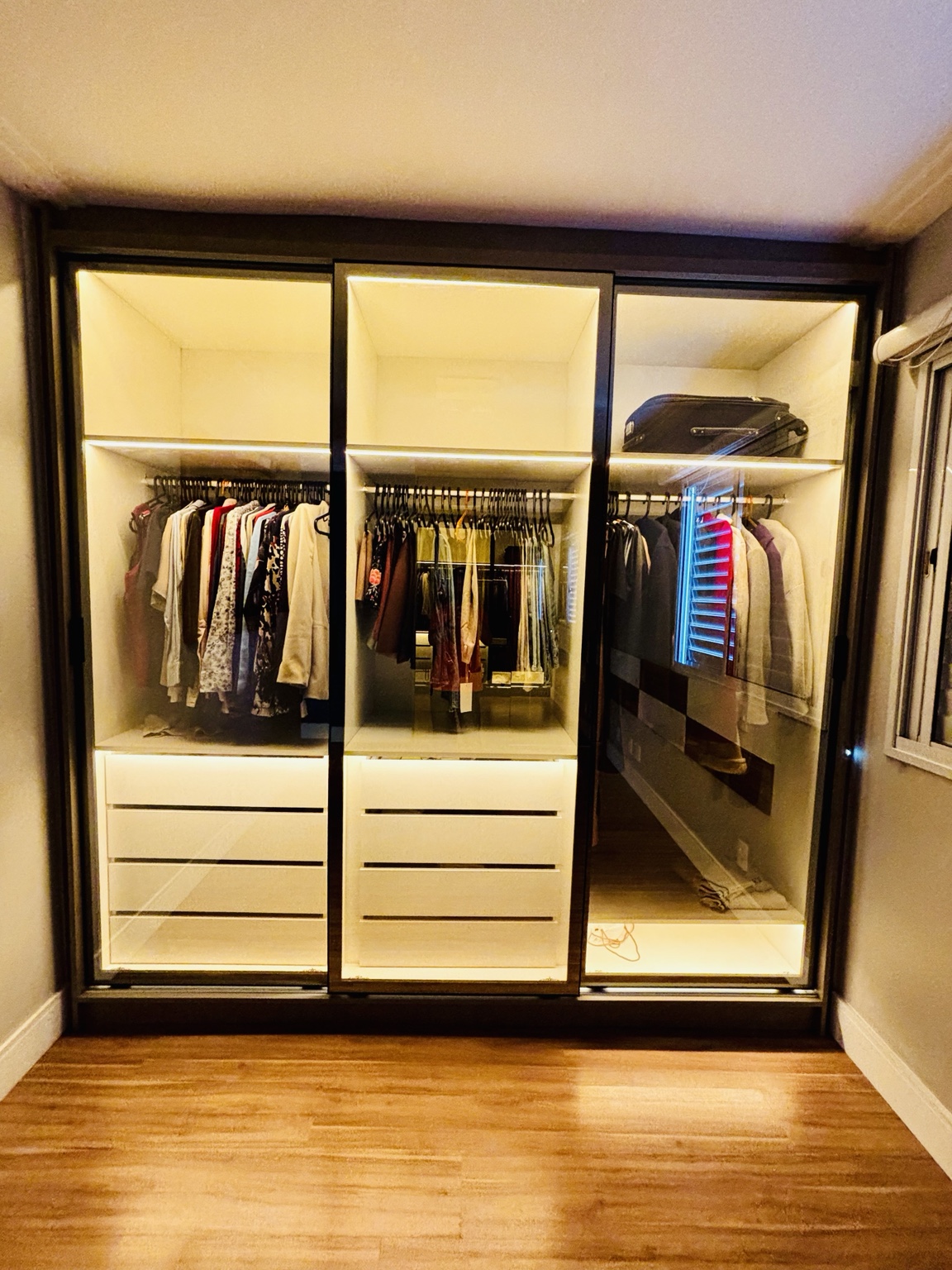 Closet planejado com portas de vidro reflecta, gaveteiros e iluminação em LED
