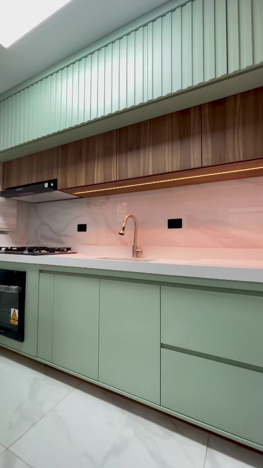 Cozinha planejada verde mint com armários amadeirados, ripado e iluminação em LED